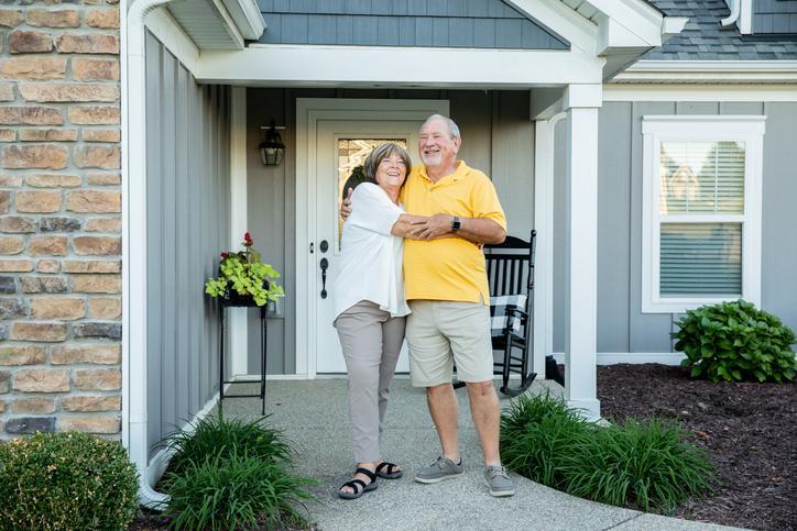 An older couple hugging outside the home they just refinanced.